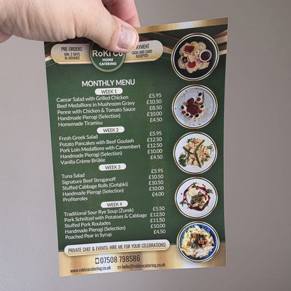 Hand holding a green A5 menu card with food items and prices on a gray background